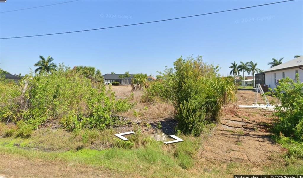 A vacant, overgrown residential lot with shrubs and trees under a clear blue sky — 15610 VISCOUNT CIRCLE, PORT CHARLOTTE, FL