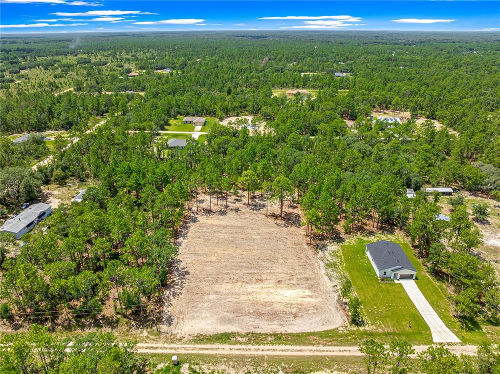 An aerial view shows a cleared rectangular lot situated between two houses and dense forest — TBD SW 90 PLACE, DUNNELLON, FL