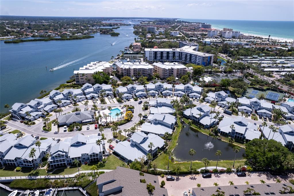 An aerial view shows a waterfront residential complex with multiple buildings, a pool, and a pond — 1220 SIESTA BAYSIDE DRIVE UNIT 1220-A, SARASOTA, FL