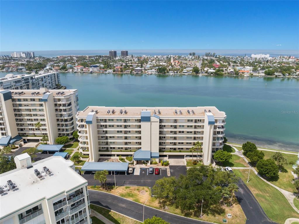 An aerial view shows a multi-story apartment building situated along a waterfront with parking areas — 7984 SAILBOAT KEY BOULEVARD S UNIT 306, SOUTH PASADENA, FL