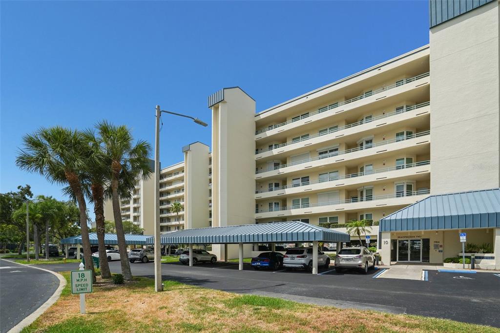 A multi-story apartment building features covered parking, palm trees, and a speed limit sign — 7984 SAILBOAT KEY BOULEVARD S UNIT 306, SOUTH PASADENA, FL