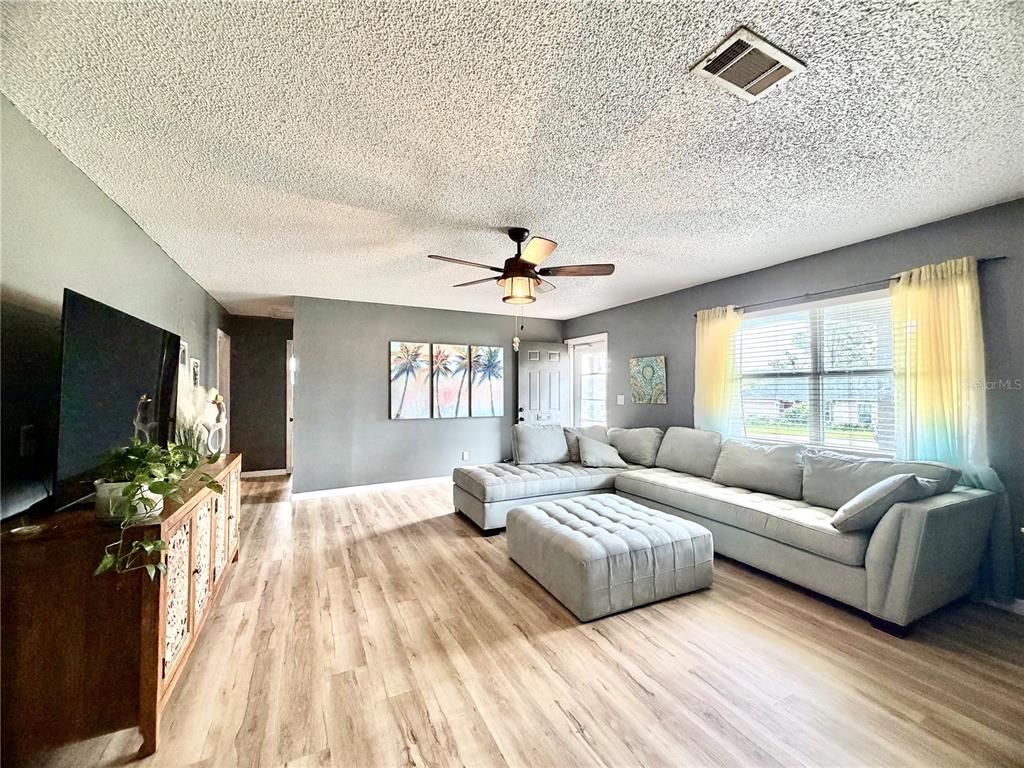 A living room features light wood-look flooring, gray walls, a sectional sofa, and a ceiling fan — 4263 WELDON AVENUE, SPRING HILL, FL