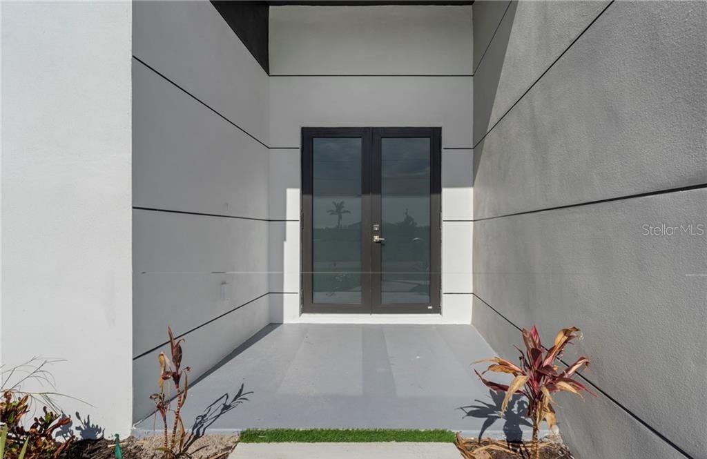 A modern entryway features double glass doors set between white walls with horizontal black accents — 4233 JACARANDA PARKWAY W, CAPE CORAL, FL