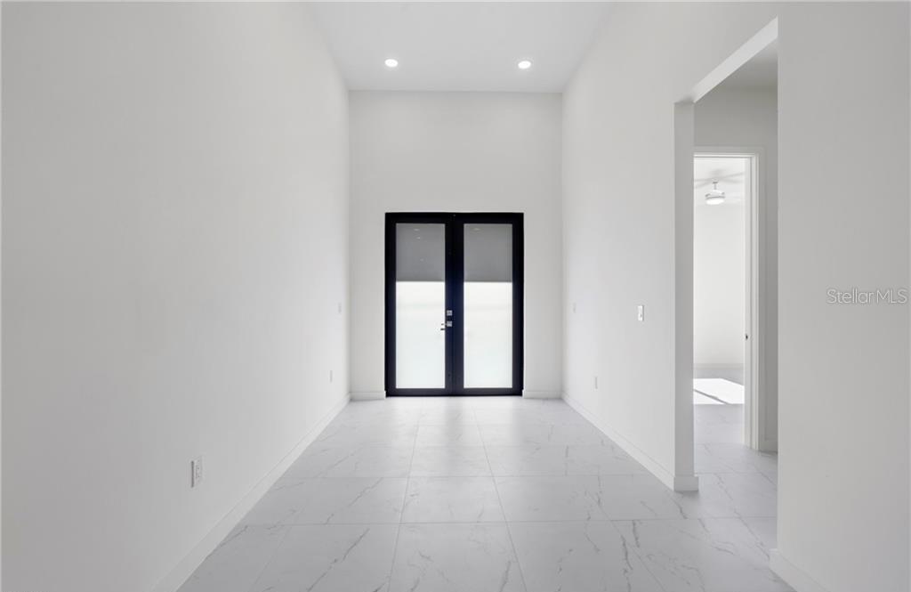 A minimalist room with white walls, marble-look tile flooring, and black-framed double glass doors — 4233 JACARANDA PARKWAY W, CAPE CORAL, FL