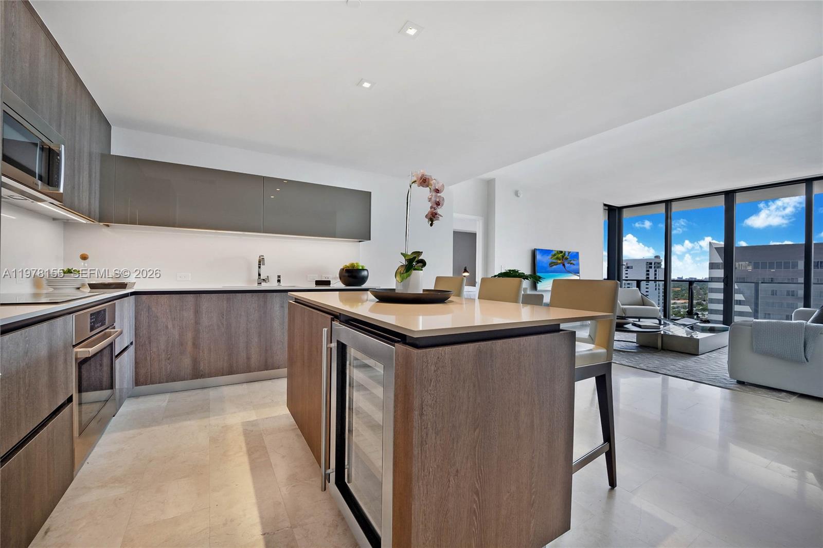 A modern kitchen with wood cabinetry and a central island overlooks a bright living area — 88 SW 7th St # 1810, Miami FL 33130, MIAMI, FL