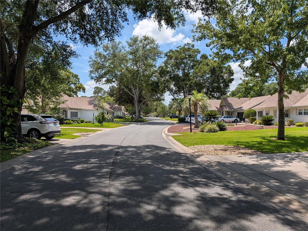 A quiet residential street lined with houses, mature trees, and parked cars under a blue sky — 8569 SW 92ND LANE UNIT B, OCALA, FL