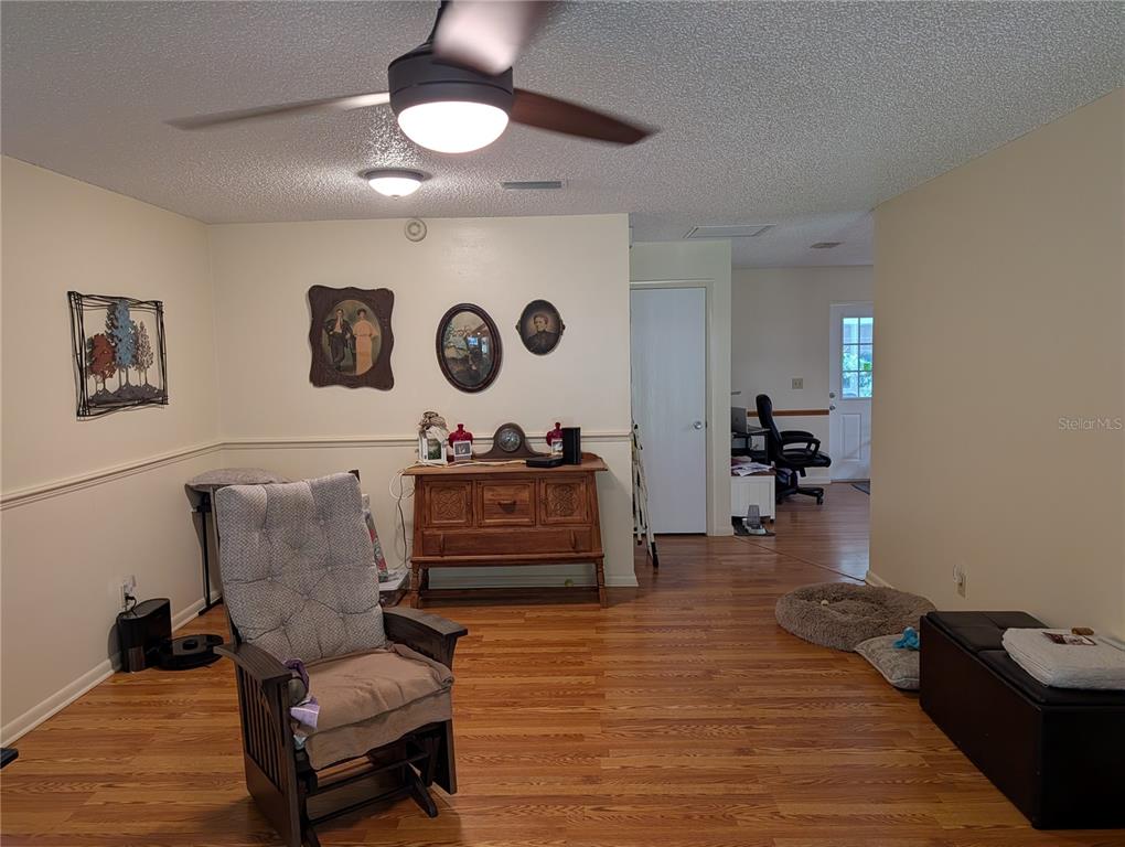 A living room features wood-look flooring, a ceiling fan, and a wooden cabinet against a wall — 8569 SW 92ND LANE UNIT B, OCALA, FL