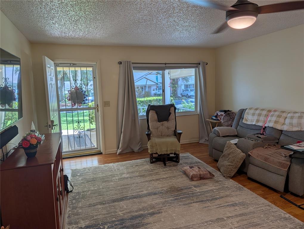A living room with a ceiling fan, a large area rug, and a front door — 8569 SW 92ND LANE UNIT B, OCALA, FL