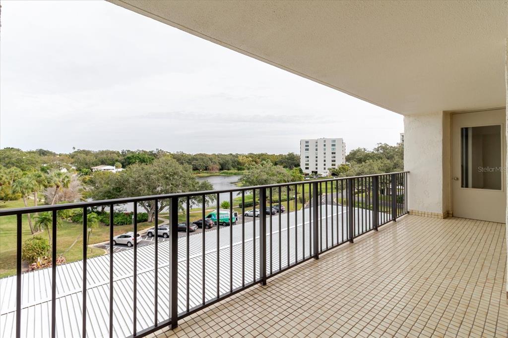 A tiled balcony with a black metal railing overlooks a parking lot and pond — 100 OAKMONT LANE UNIT 507, BELLEAIR, FL