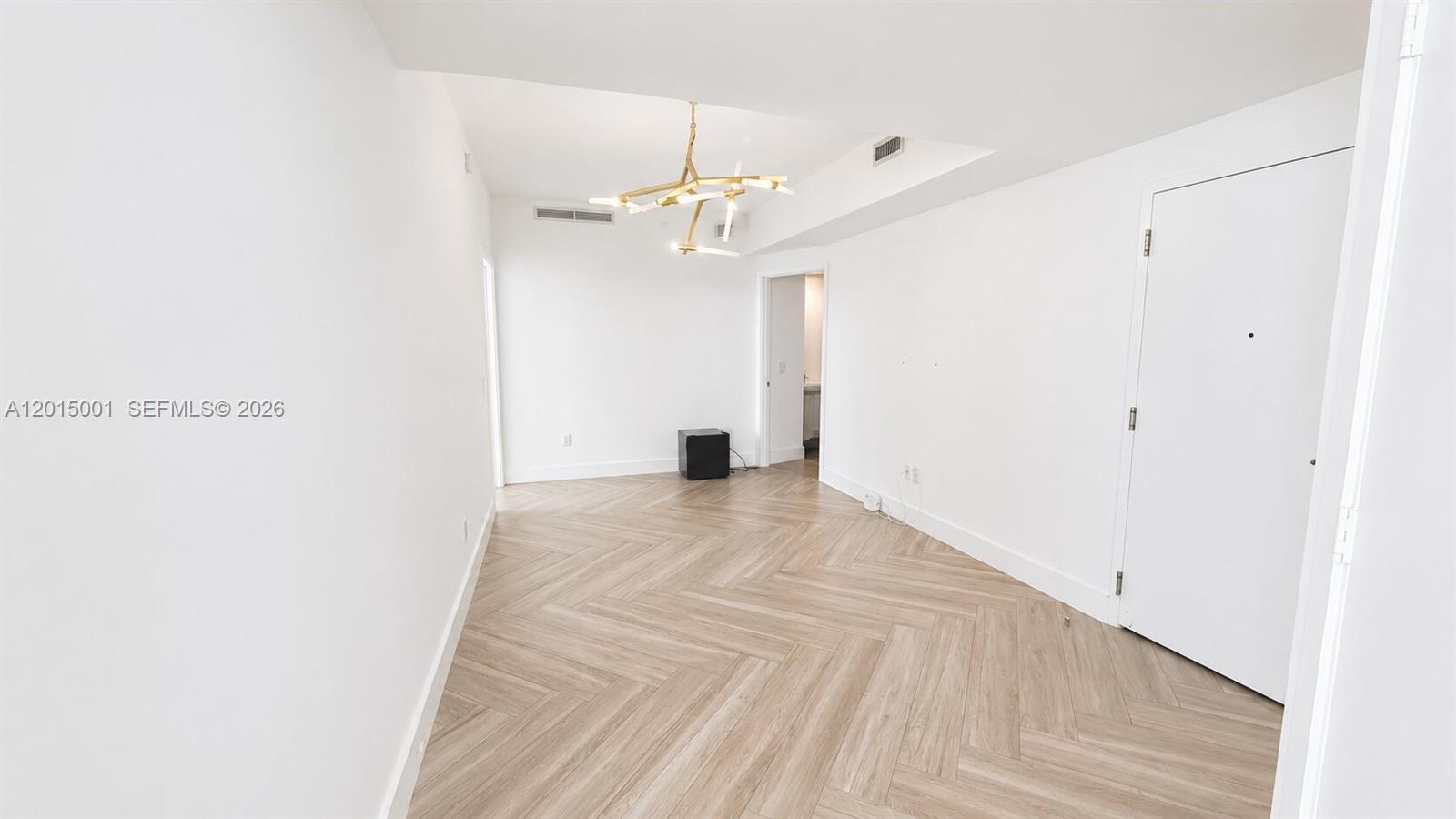 A bright, empty room features white walls, light wood herringbone flooring, and a modern chandelier — 2900 NE 7th Ave # 3207, Miami FL 33137, MIAMI, FL