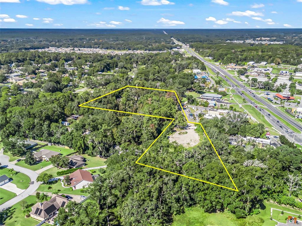An aerial view shows a wooded lot outlined in yellow near a highway and houses — 10366 S US HIGHWAY 441, BELLEVIEW, FL