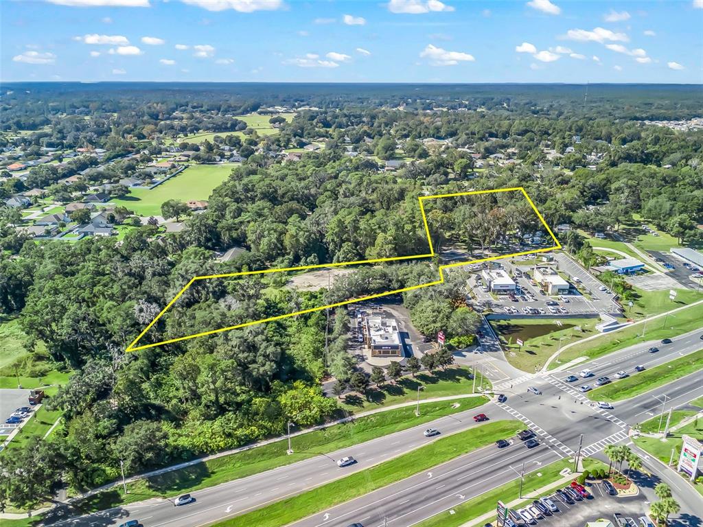 An aerial view shows a wooded lot outlined in yellow adjacent to commercial buildings — 10366 S US HIGHWAY 441, BELLEVIEW, FL