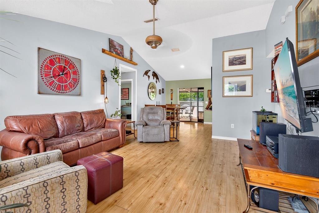A living room features a leather sofa, patterned armchair, wood-look flooring, and a television — 5610 33RD LANE E, BRADENTON, FL