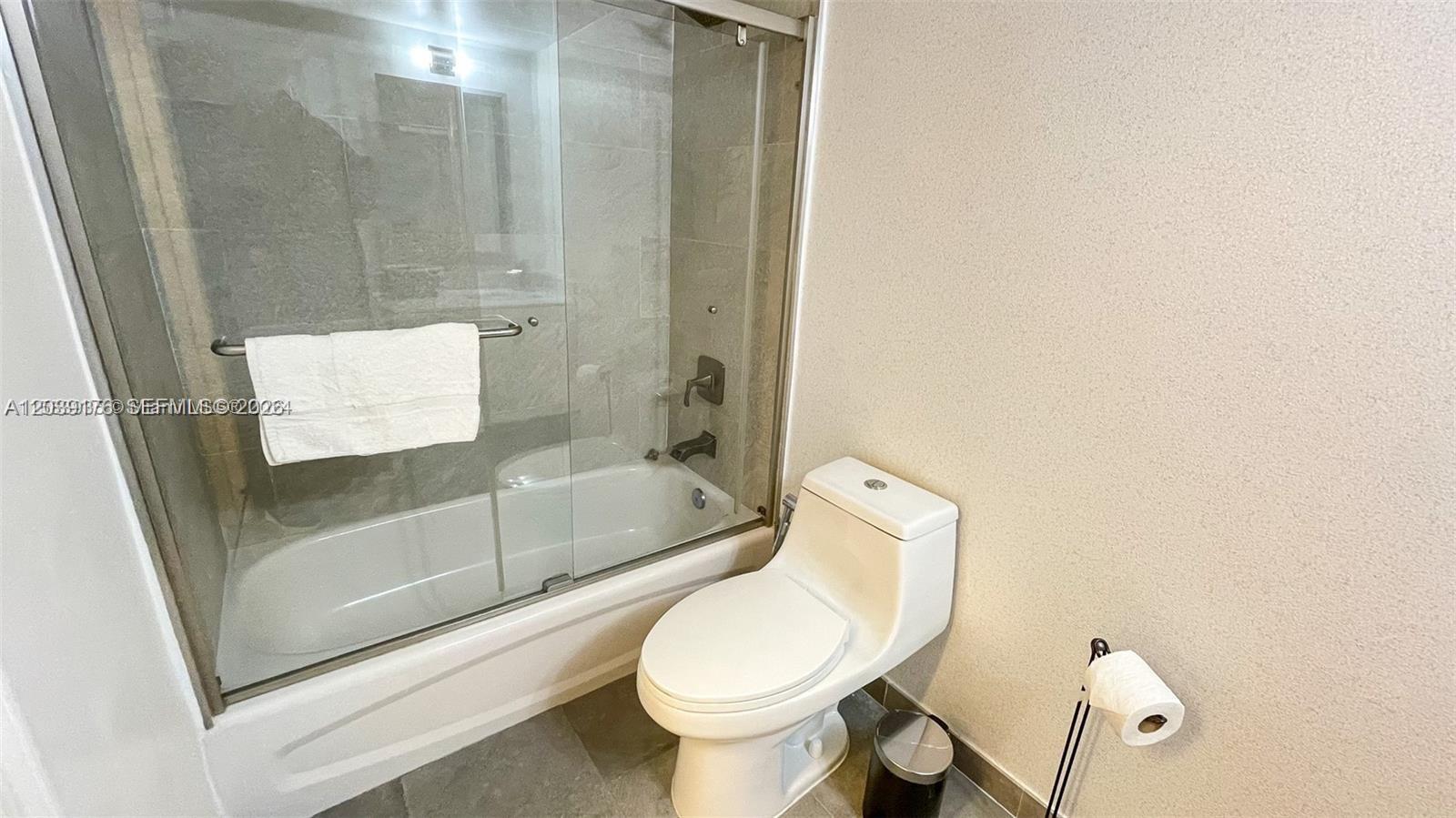 A bathroom features a white toilet, a glass-enclosed bathtub, and a wall-mounted toilet paper holder — 1200 Brickell Bay Dr # 1702, Miami FL 33131, MIAMI, FL