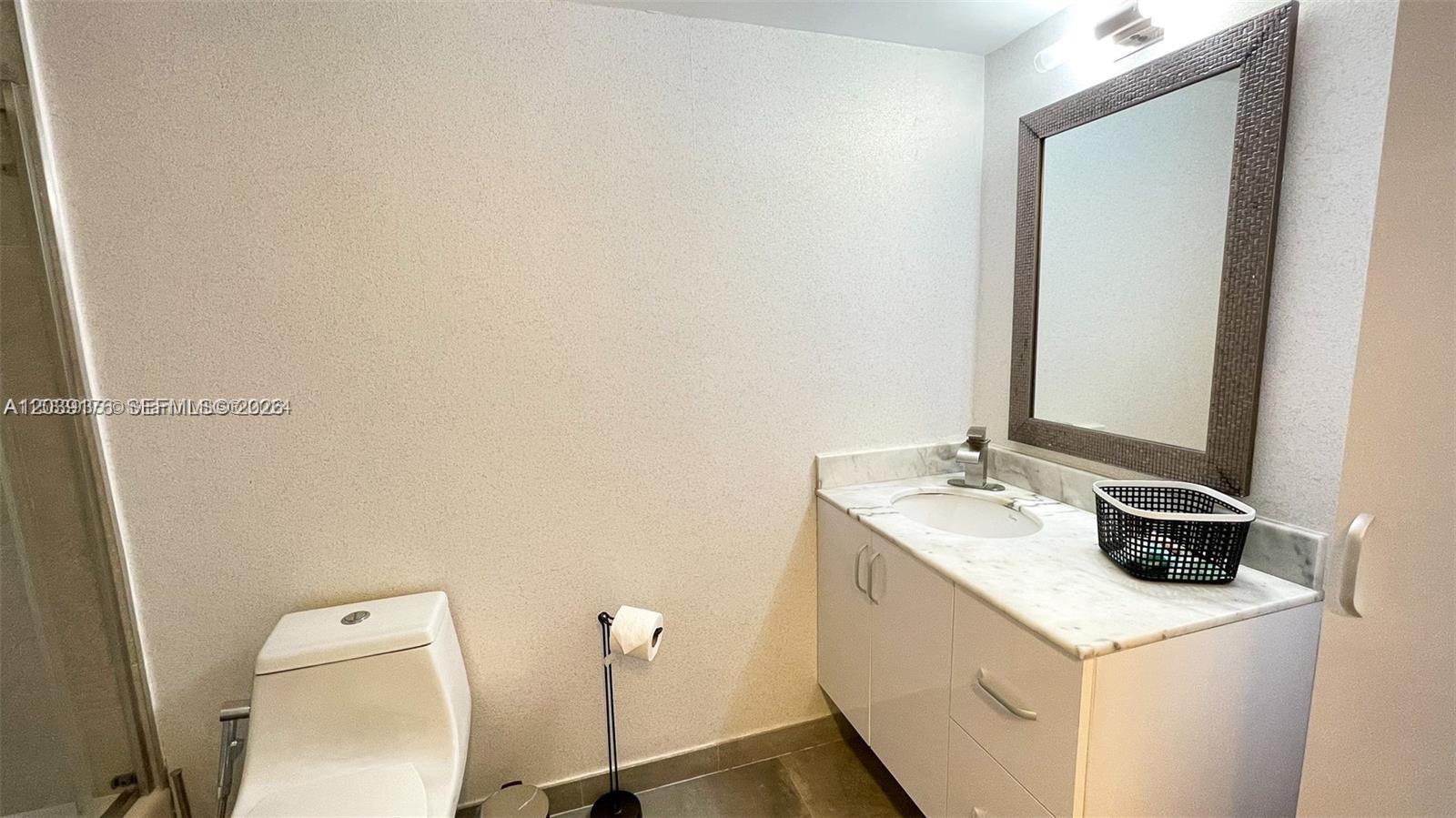 A bathroom features a white vanity with a marble countertop, a toilet, and a framed mirror — 1200 Brickell Bay Dr # 1702, Miami FL 33131, MIAMI, FL