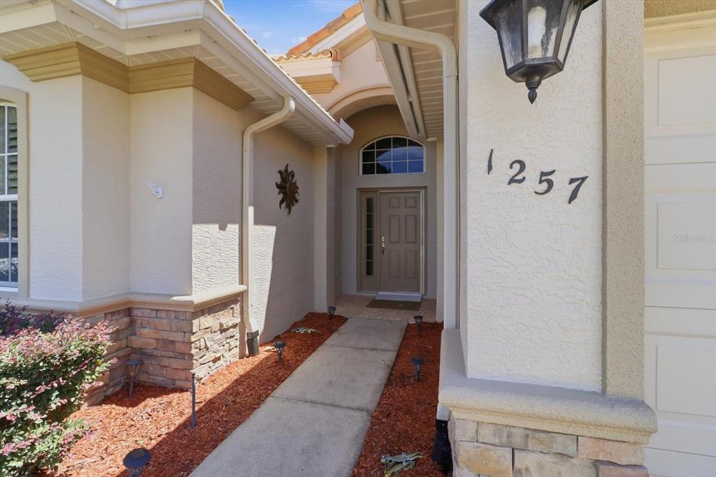 A concrete walkway leads to the front entrance of a house with tan stucco siding — 1257 W SKYVIEW CROSSING DRIVE, HERNANDO, FL