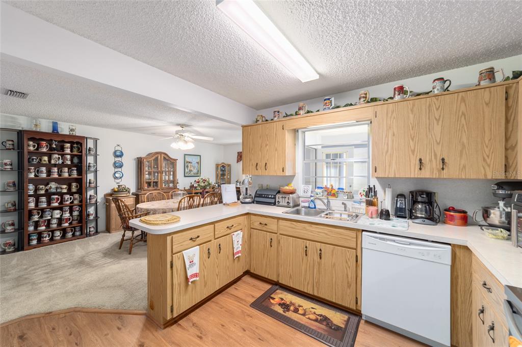 A kitchen with oak cabinets and a white dishwasher opens into a carpeted dining area — 9233 SW 83RD TERRACE UNIT D, OCALA, FL