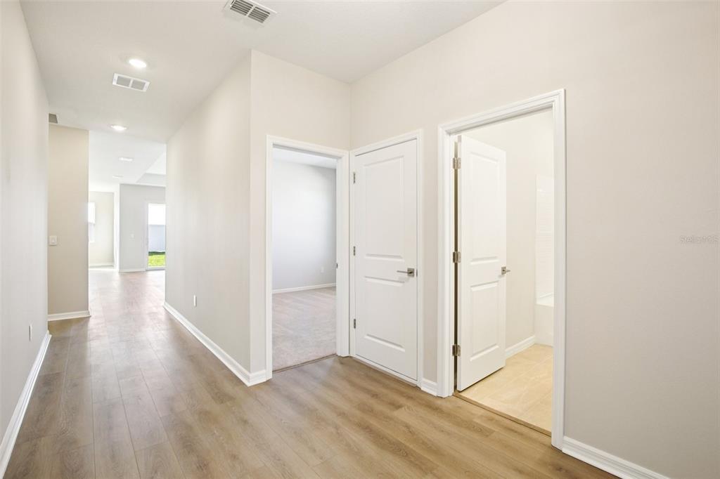 A hallway with wood-look flooring leads to a bedroom and a bathroom with white doors — 5911 FRESH FLORA DRIVE, WIMAUMA, FL
