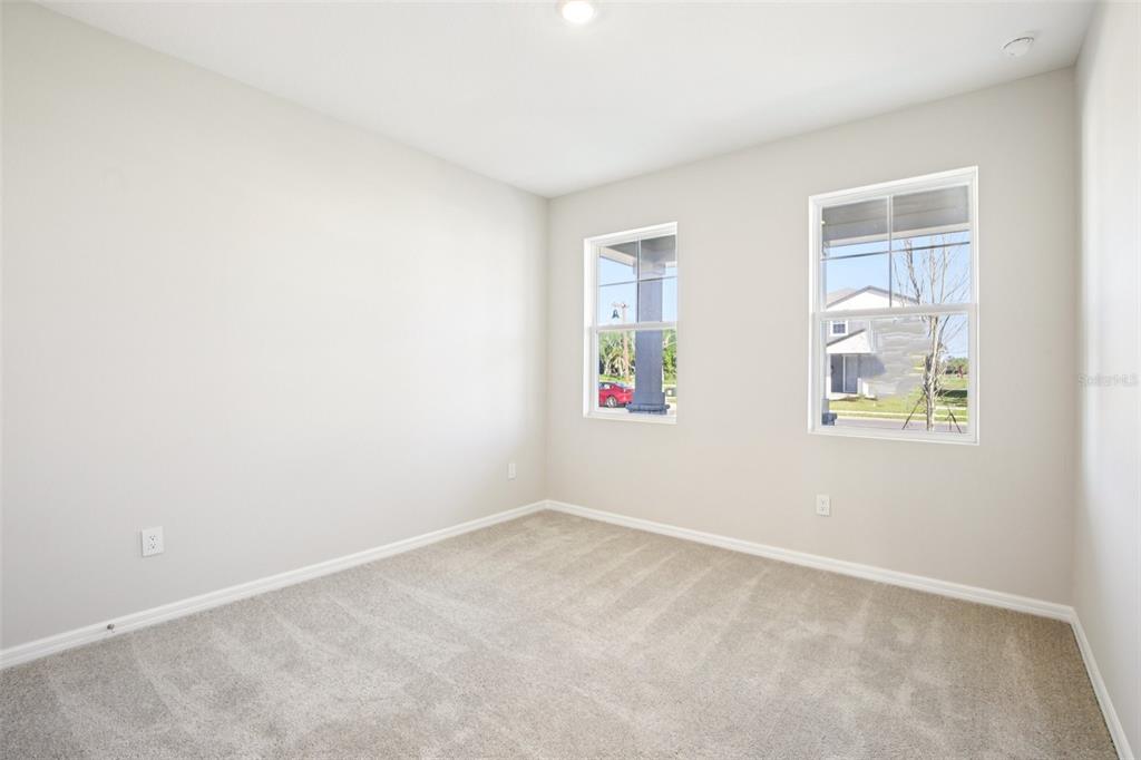 An empty bedroom features light-colored walls, beige carpeting, and two windows overlooking a neighborhood — 5911 FRESH FLORA DRIVE, WIMAUMA, FL