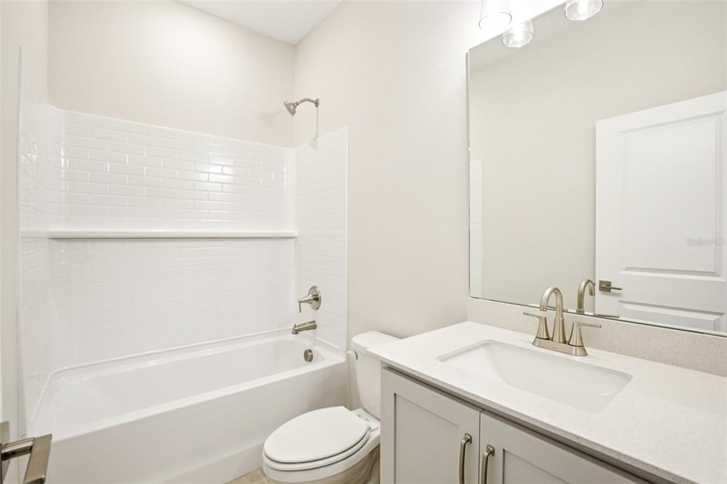 A bathroom features a white subway tile shower-tub combo, a gray vanity, and a mirror — 5911 FRESH FLORA DRIVE, WIMAUMA, FL