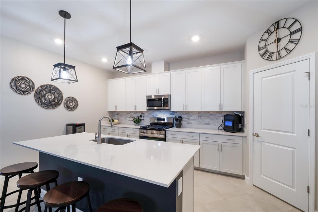 A modern kitchen features white cabinetry, a large island with a sink, and pendant lighting — 15041 SERENE SHORES LOOP, BRADENTON, FL