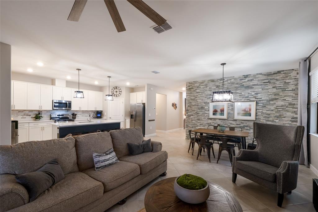 An open-concept living and dining area features a stone accent wall and a kitchen island — 15041 SERENE SHORES LOOP, BRADENTON, FL