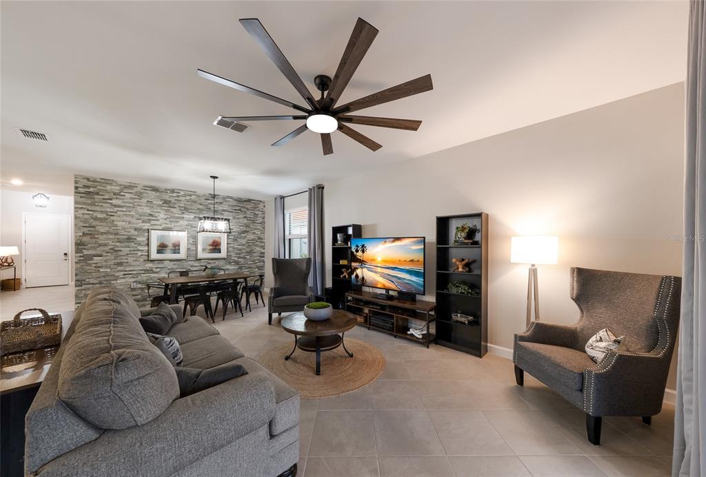 A living room features a stone accent wall, gray furniture, and a large ceiling fan — 15041 SERENE SHORES LOOP, BRADENTON, FL