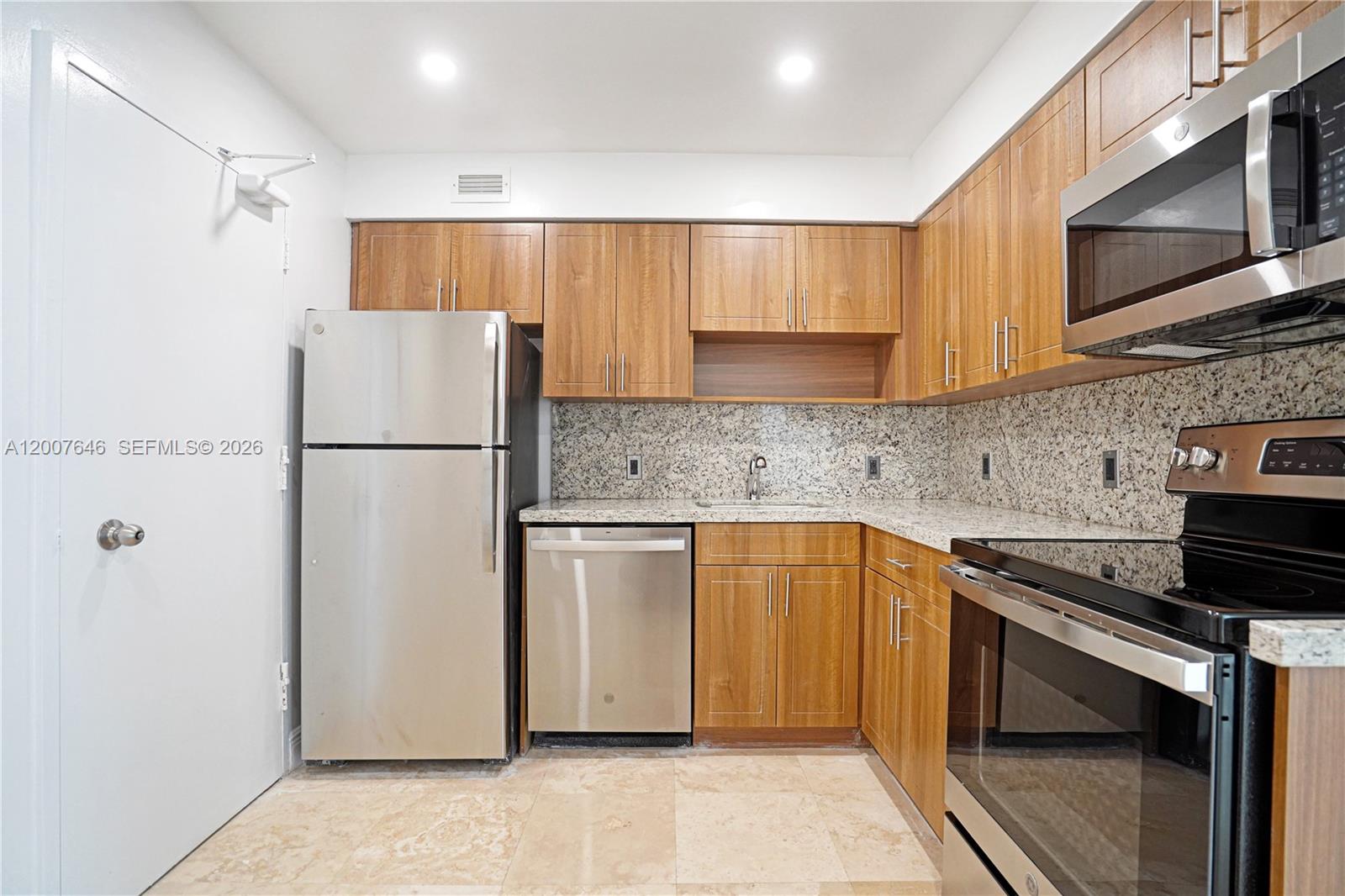 A kitchen features wood cabinets, granite countertops, stainless steel appliances, and tile flooring — 5101 Collins Ave # 14F, Miami Beach FL 33140, MIAMI BEACH, FL