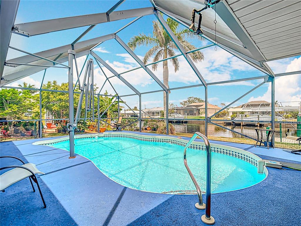 A screened-in swimming pool overlooks a canal with a palm tree and neighboring houses — 18790 COUNTRYMAN AVENUE, PORT CHARLOTTE, FL