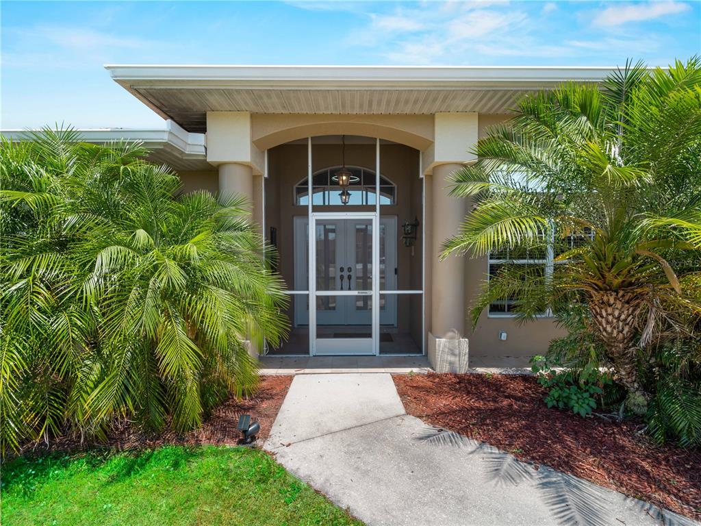 A concrete walkway leads to a covered entryway with a screened door and two columns — 2288 PRAGUE LANE, PUNTA GORDA, FL