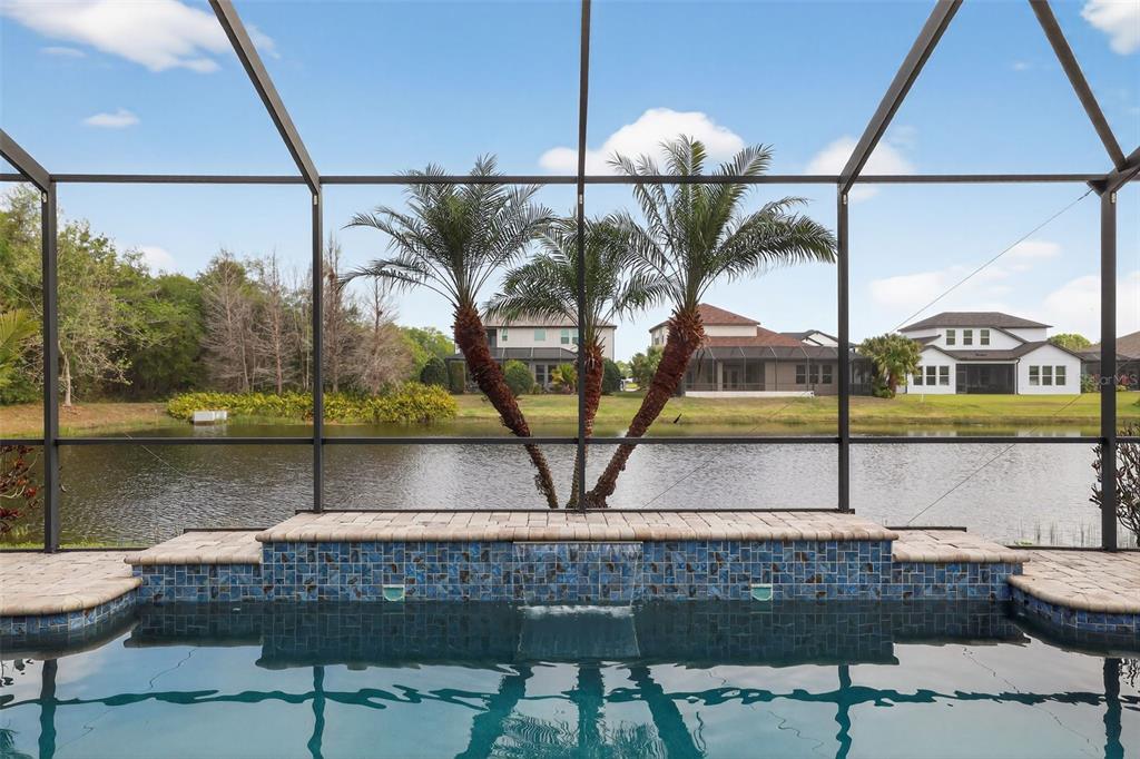 A swimming pool with a tiled water feature overlooks a lake and neighboring houses — 710 116TH COURT NE, BRADENTON, FL