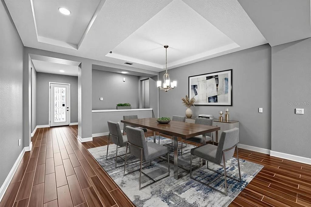 A dining room features a wooden table, gray chairs, a patterned rug, and tray ceilings — 710 116TH COURT NE, BRADENTON, FL