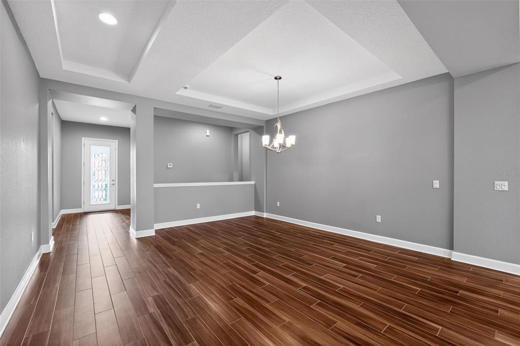 An empty dining room features a tray ceiling, a chandelier, and dark wood-look tile flooring — 710 116TH COURT NE, BRADENTON, FL