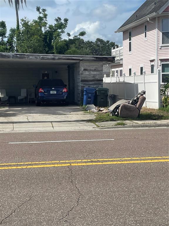 A blue car is parked under a carport next to trash bins and a discarded chair — 2445 WEBBER STREET, SARASOTA, FL