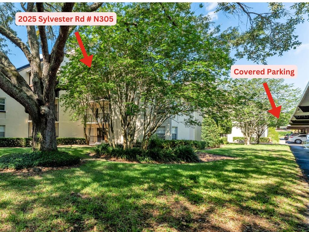 An exterior view of a multi-story apartment building with trees and a covered parking area — 2025 SYLVESTER RD UNIT N305, LAKELAND, FL