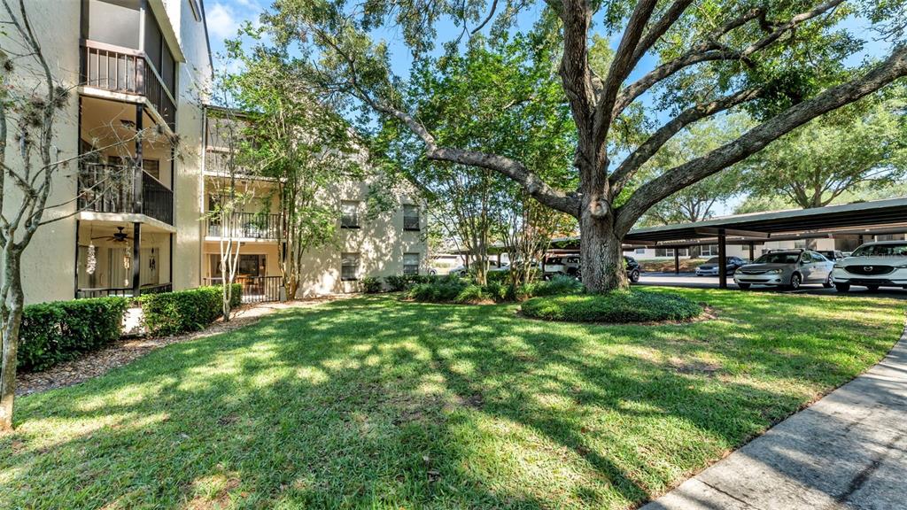 A multi-story apartment building with balconies stands next to a lawn and covered parking — 2025 SYLVESTER RD UNIT N305, LAKELAND, FL