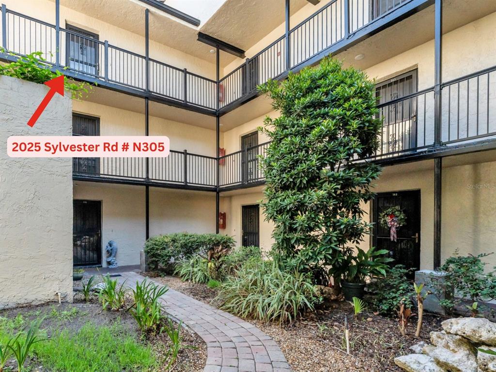 An exterior view of a multi-story apartment building with open walkways and a landscaped courtyard — 2025 SYLVESTER RD UNIT N305, LAKELAND, FL