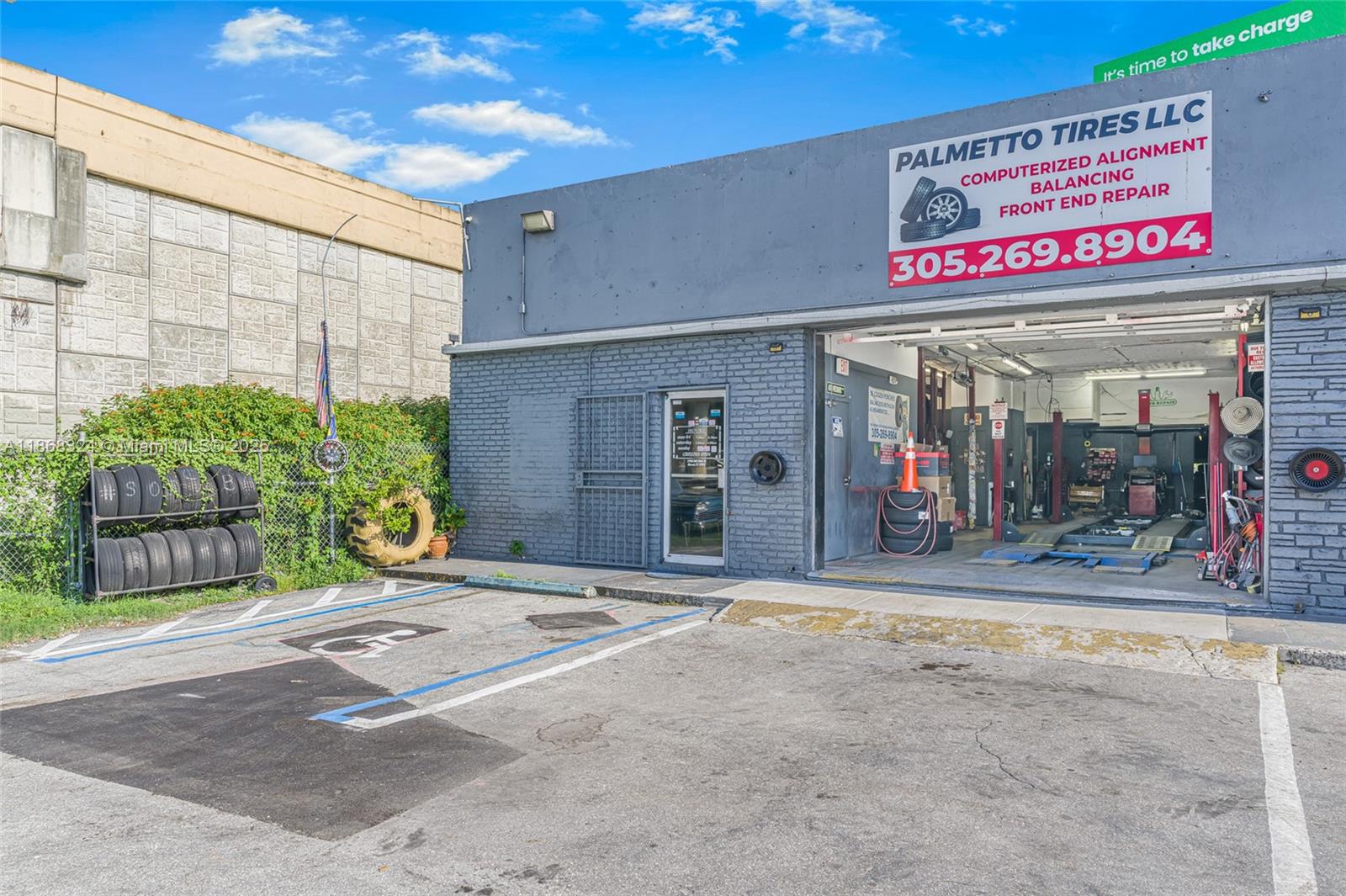 The exterior of a gray brick automotive repair shop features a tire rack and parking space — 7790 SW 26th St, Miami FL 33155, MIAMI, FL