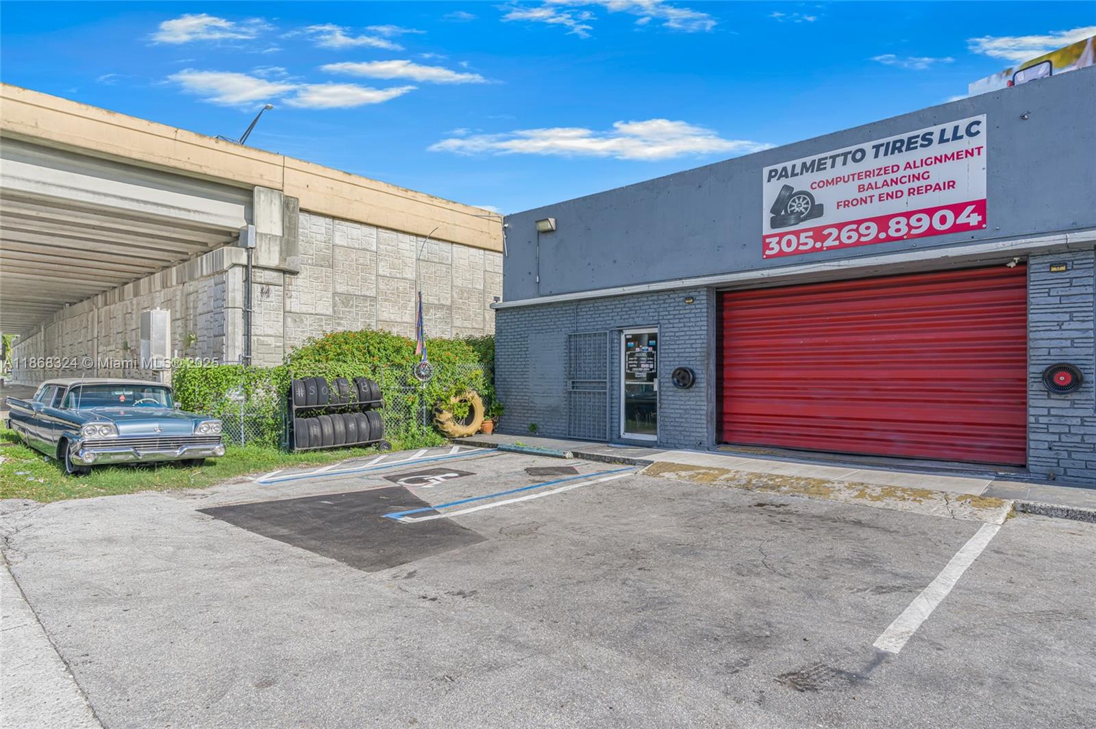 An exterior view of a tire shop with a red roll-up door and parking — 7790 SW 26th St, Miami FL 33155, MIAMI, FL