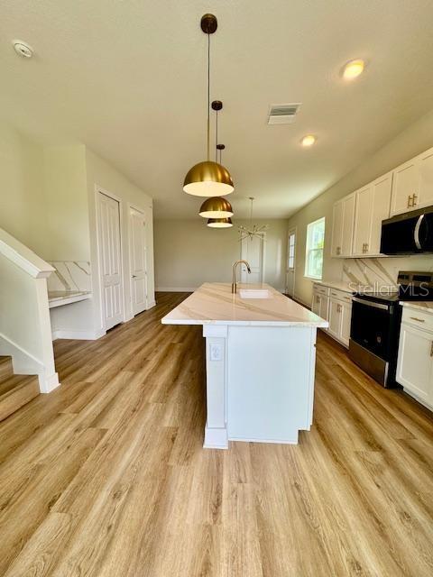 A modern kitchen features a white island with pendant lighting, light wood flooring, and white cabinetry — 1600 BIRCHFIELD COVE, OVIEDO, FL