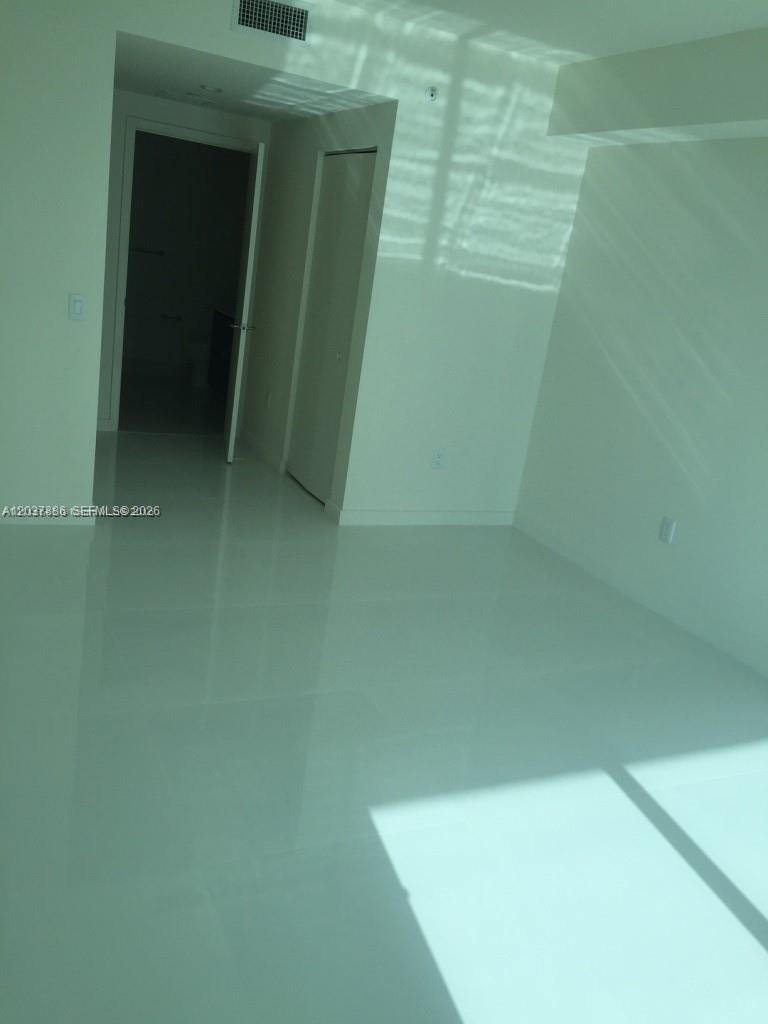 An empty room with white walls, glossy tile flooring, and a doorway leading to a bathroom — 1100 S MIAMI AVE # 3811, Miami FL 33130, MIAMI, FL