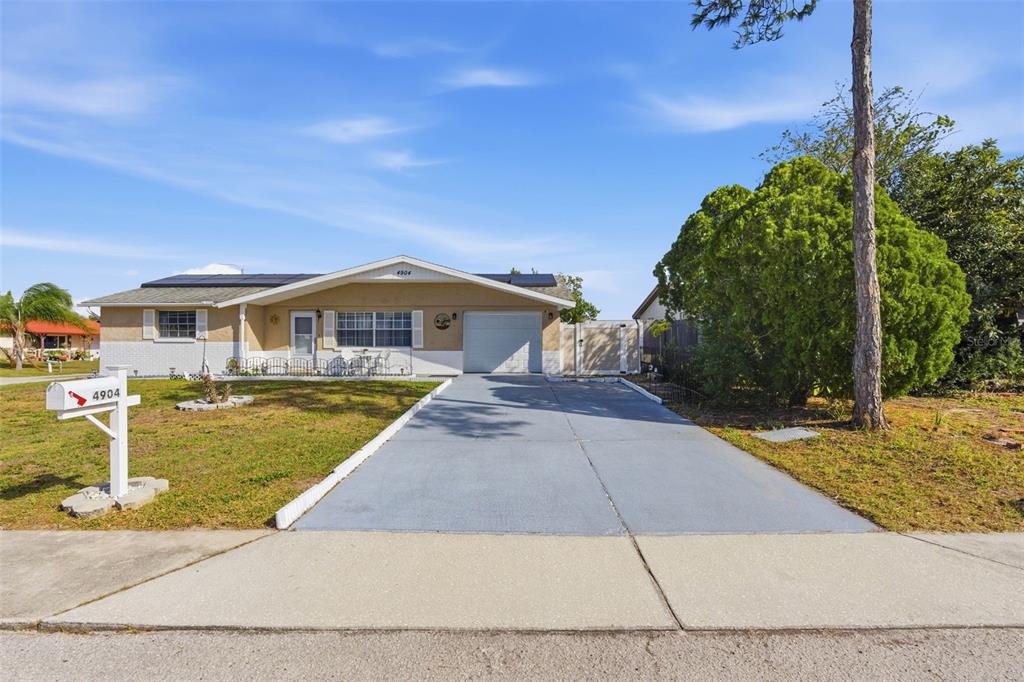 A single-story house with a tan exterior, a concrete driveway, and a large front tree — 4904 ELMWOOD STREET, NEW PORT RICHEY, FL