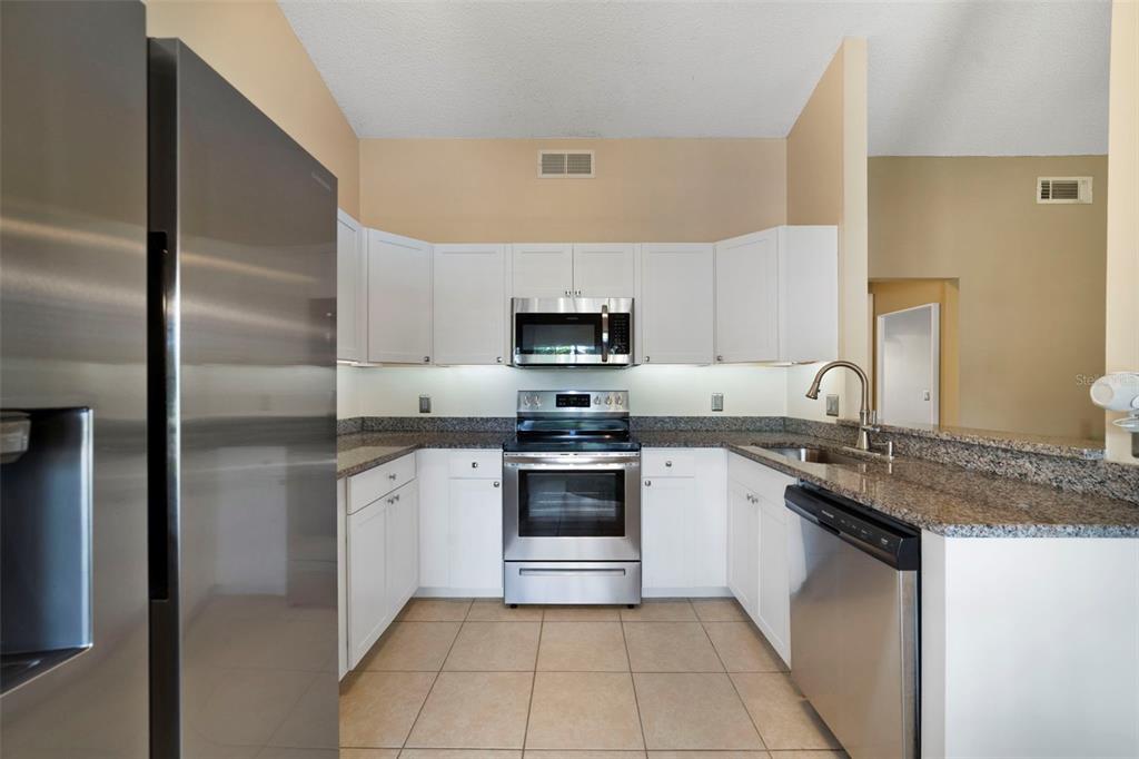 A kitchen features white cabinets, stainless steel appliances, and granite countertops over tile flooring — 13953 FOX MEADOW DRIVE, ORLANDO, FL
