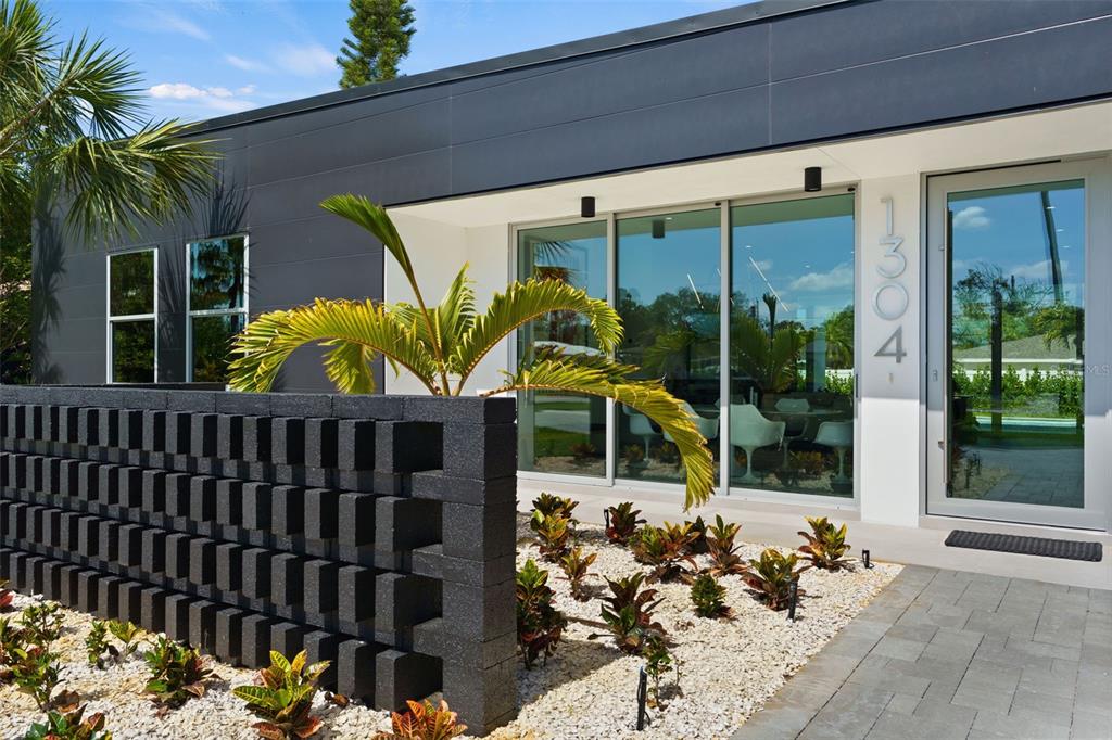 A modern home exterior features a dark block wall, gravel landscaping, and large glass doors — 1304 INDIAN ROCKS ROAD, BELLEAIR, FL