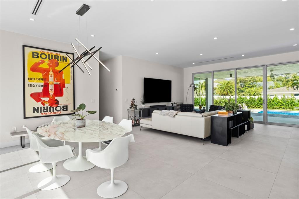 A modern open-concept living and dining area features a marble table, white chairs, and large sliding glass doors — 1304 INDIAN ROCKS ROAD, BELLEAIR, FL