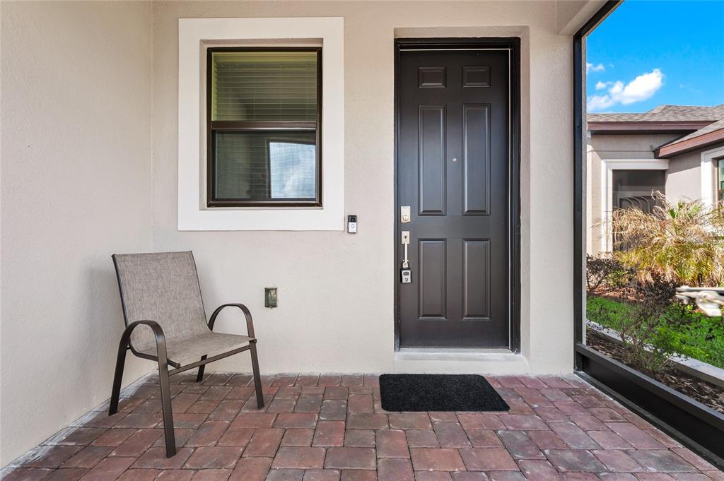 A patio with brick pavers, a single chair, and a dark front door — 1317 LOMBARDI COURT, KISSIMMEE, FL