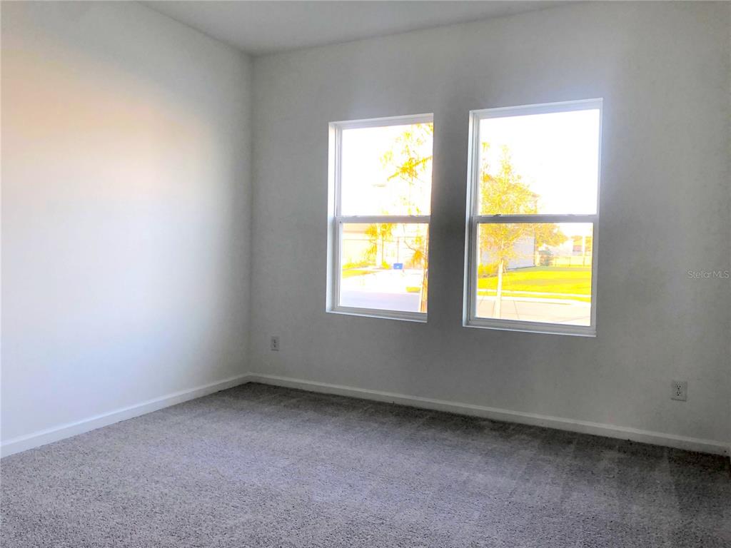 An empty bedroom features gray carpet, white walls, and two windows overlooking a neighborhood — 1314 DALKEITH CV, SANFORD, FL