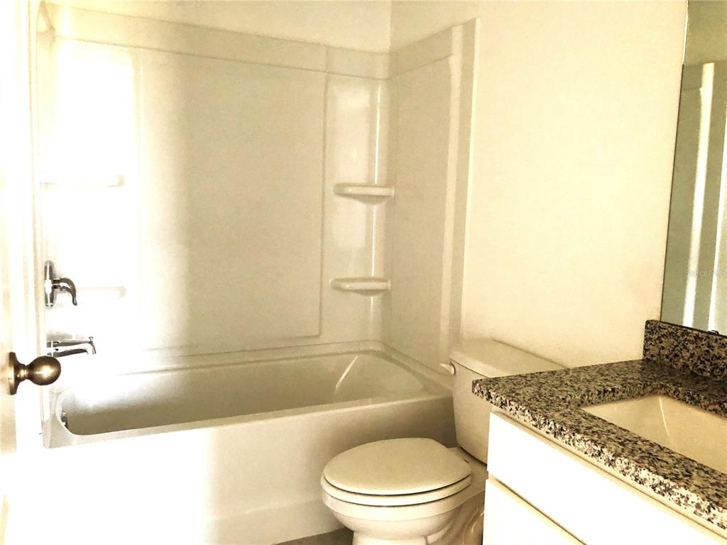 A bathroom features a white bathtub-shower combination, a toilet, and a granite-topped vanity — 1314 DALKEITH CV, SANFORD, FL