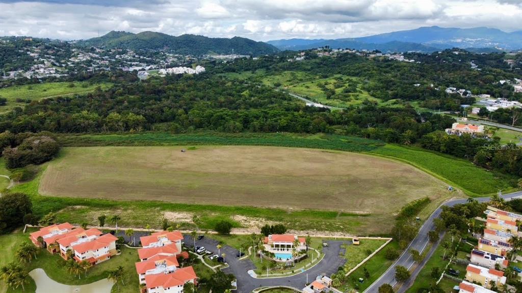 An aerial view shows a large, flat, grassy lot adjacent to a residential apartment complex — ACADEMY DRIVE, HUMACAO, PR