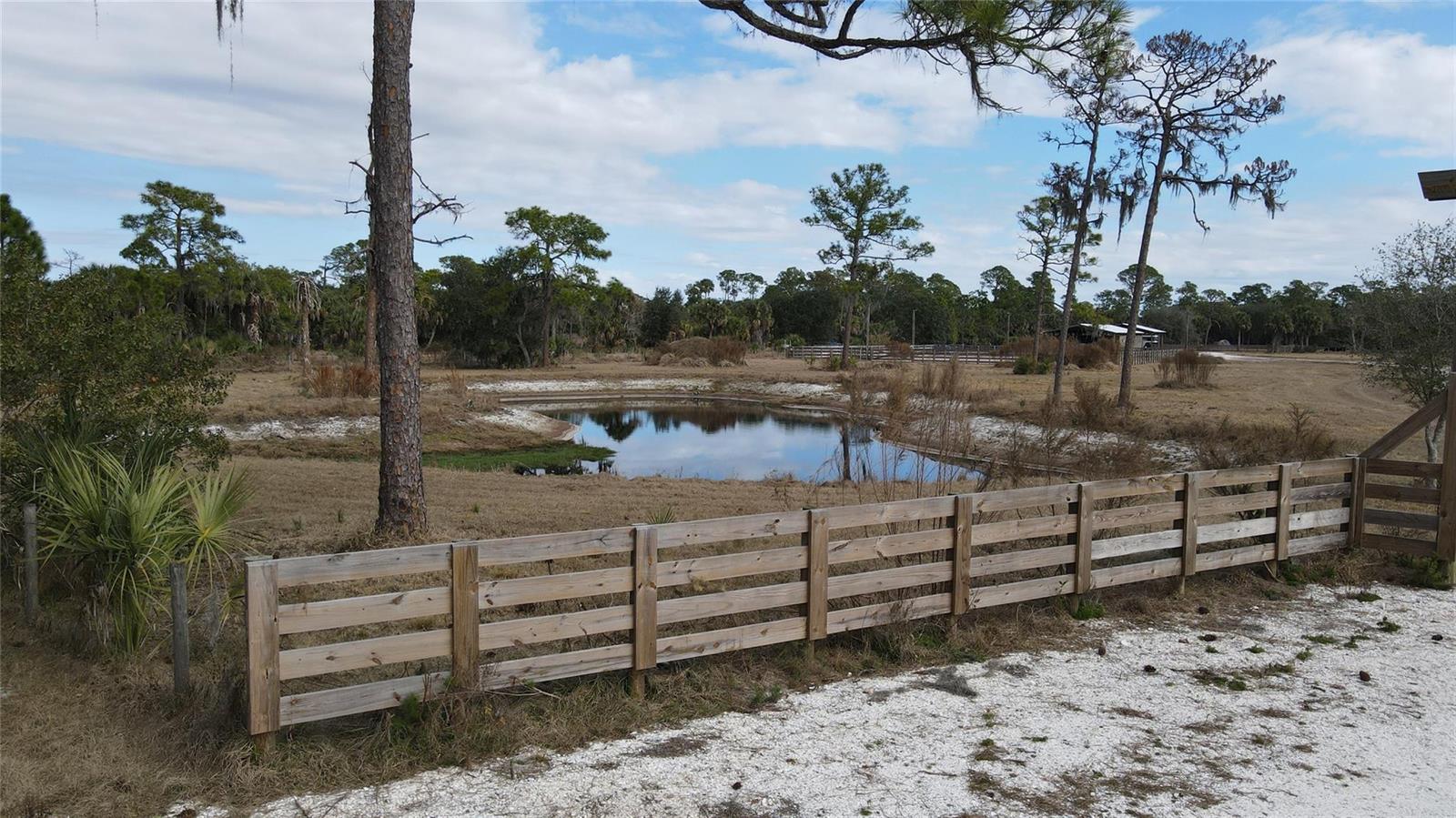 A wooden fence encloses a small pond in a grassy, tree-lined rural landscape — 4801 SW Wild Turkey Lane, Okeechobee FL 34974, OKEECHOBEE, FL